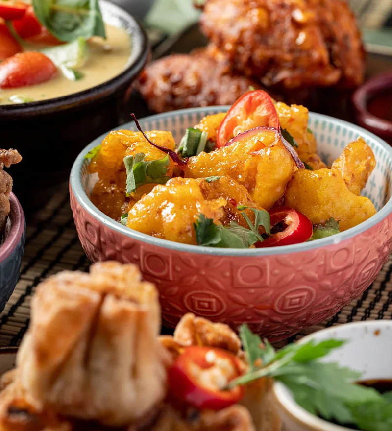 A bowl of golden battered bites with chilli and coriander, restaurant food photography by Kombu