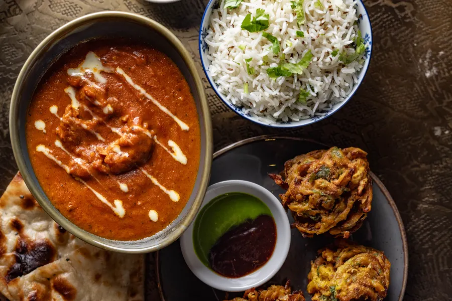 A curry with cream swirled through it, rice and onion bhajis from above